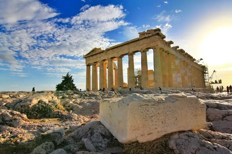 The Parthenon on the Acropolis at golden hour, its columns catching the low sun against a partly cloudy sky