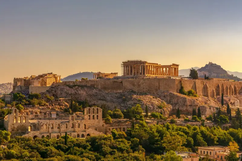 The Acropolis rock in warm, low light, with the Parthenon partly under scaffolding, the Odeon of Herodes Atticus on the slope below and Lycabettus Hill behind