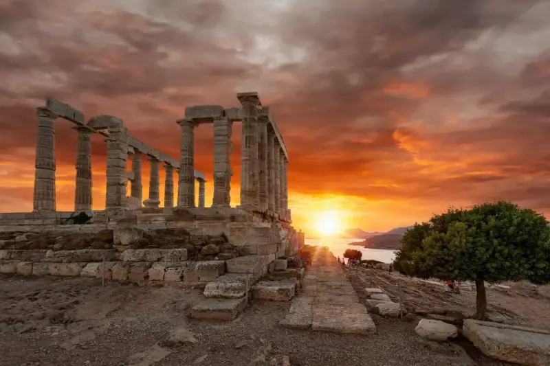 The Temple of Poseidon silhouetted against a fiery orange sunset over the sea