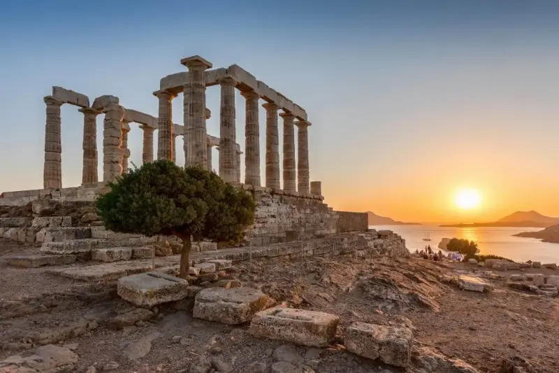 The Temple of Poseidon's columns beside a lone tree at Cape Sounion under a clear blue sky