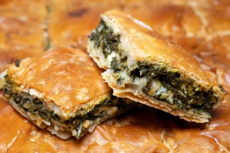 Two halves of spanakopita cut open to show the spinach and cheese filling inside flaky pastry